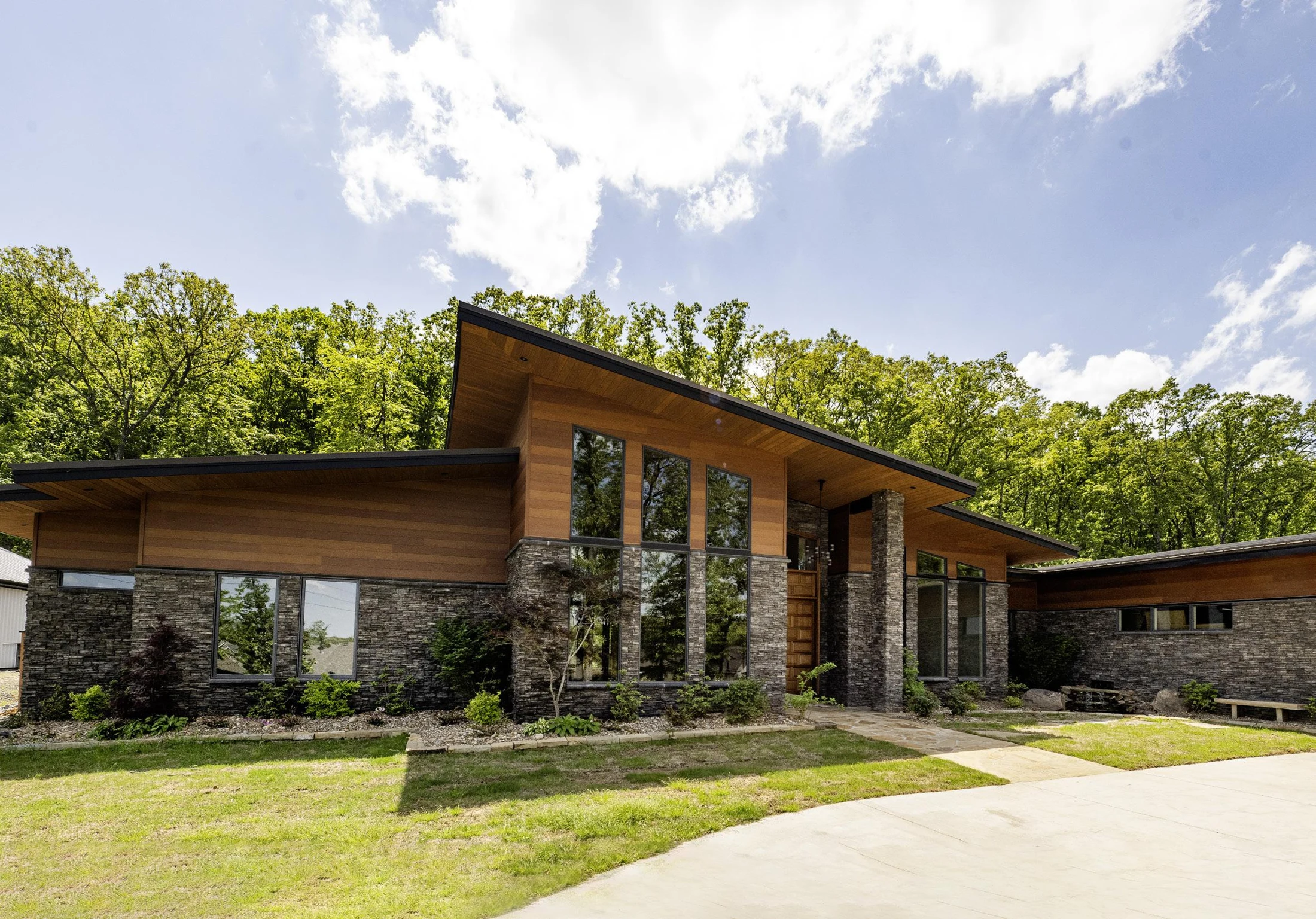 Custom midcentury-inspired home with a low roofline, stone walls, wood siding, and tall windows