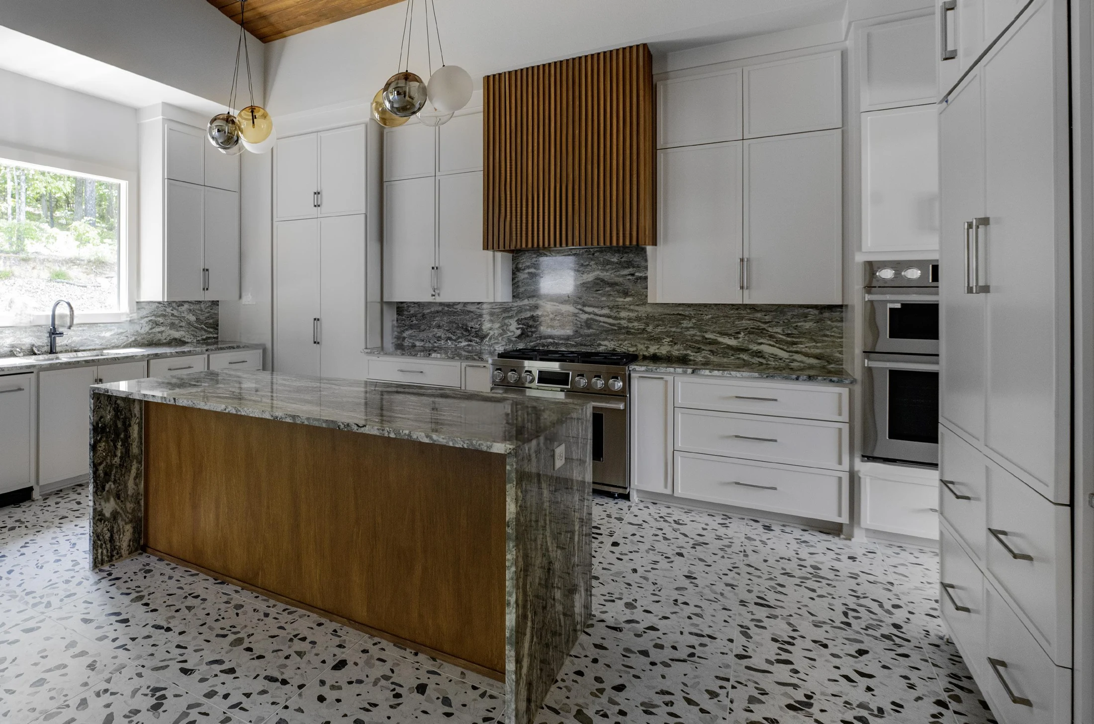 Custom kitchen with a wood island, stone counters, white cabinetry, and terrazzo flooring